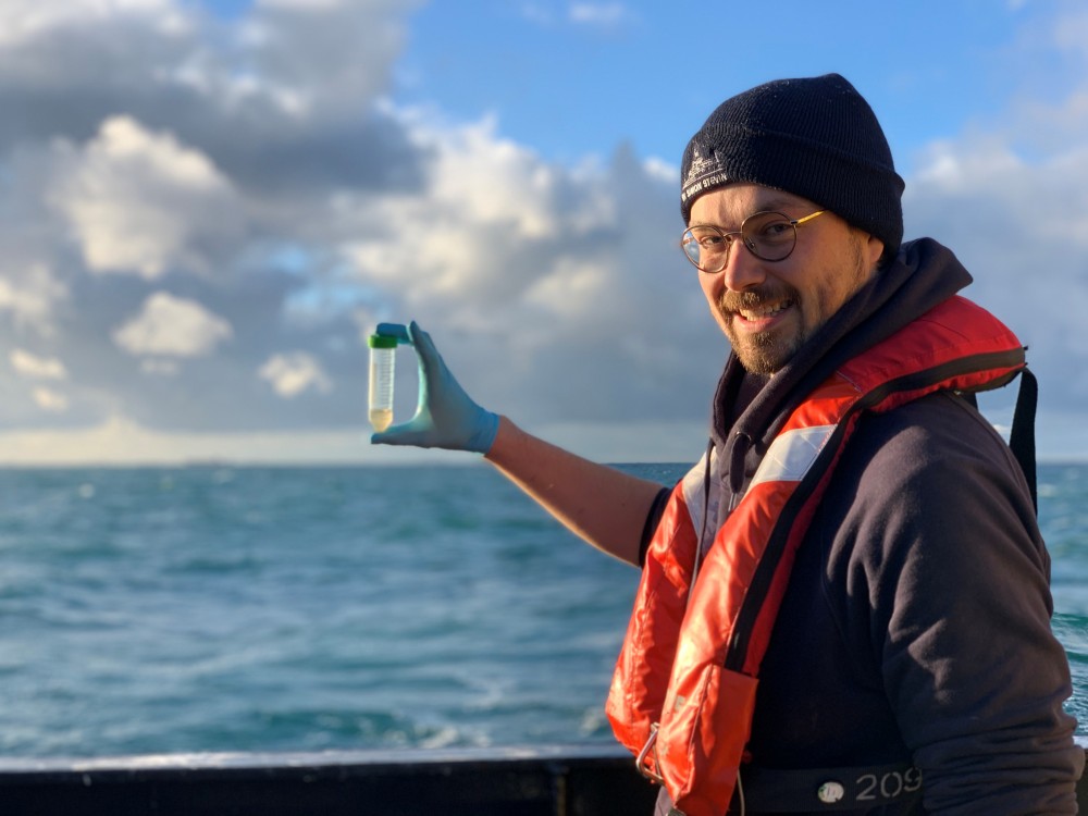Michiel Perneel aan boord van RV Simon Stevin met een waterstaal voor metagenomics analyse